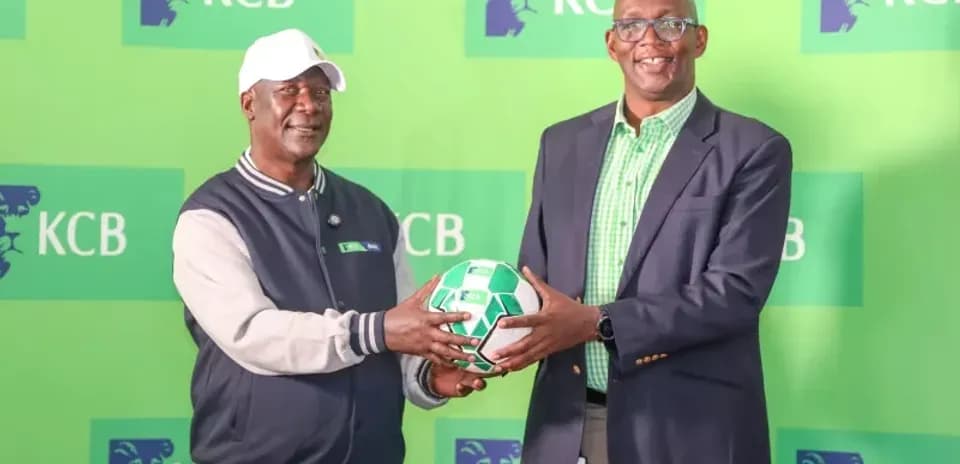 Два человека обмениваются футбольным мячом на фоне KCB