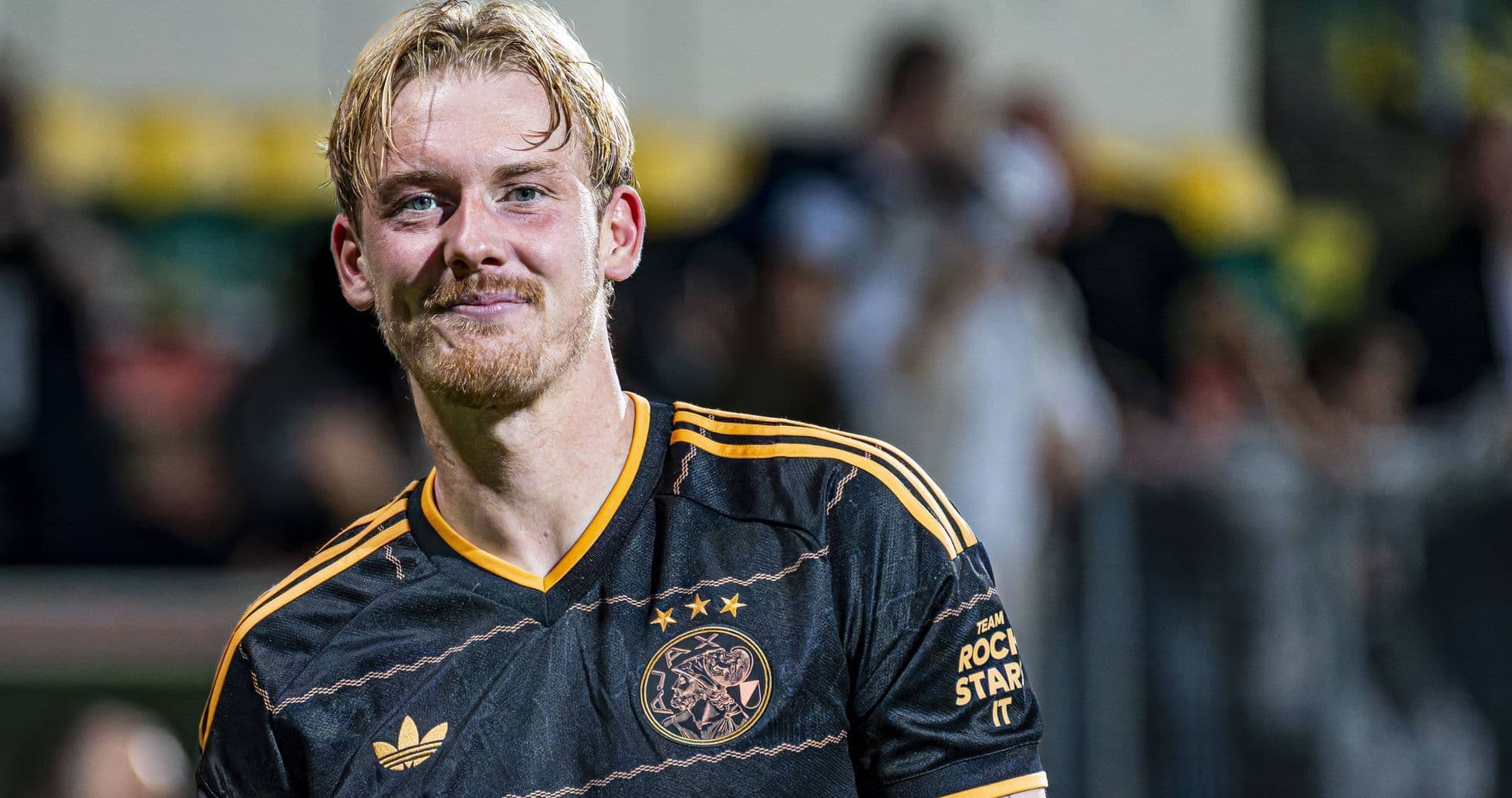 Игрок в черной форме с логотипом Ajax на поле