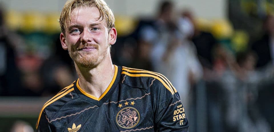 Игрок в черной форме с логотипом Ajax на поле