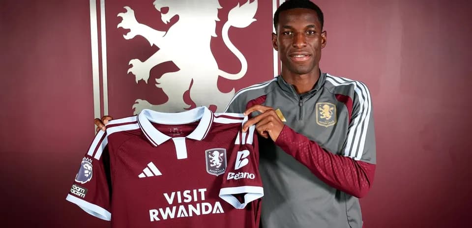 Игрок держит футболку Aston Villa на фоне логотипа