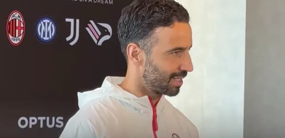 Человек в тренировочной куртке AC Milan на пресс-конференции