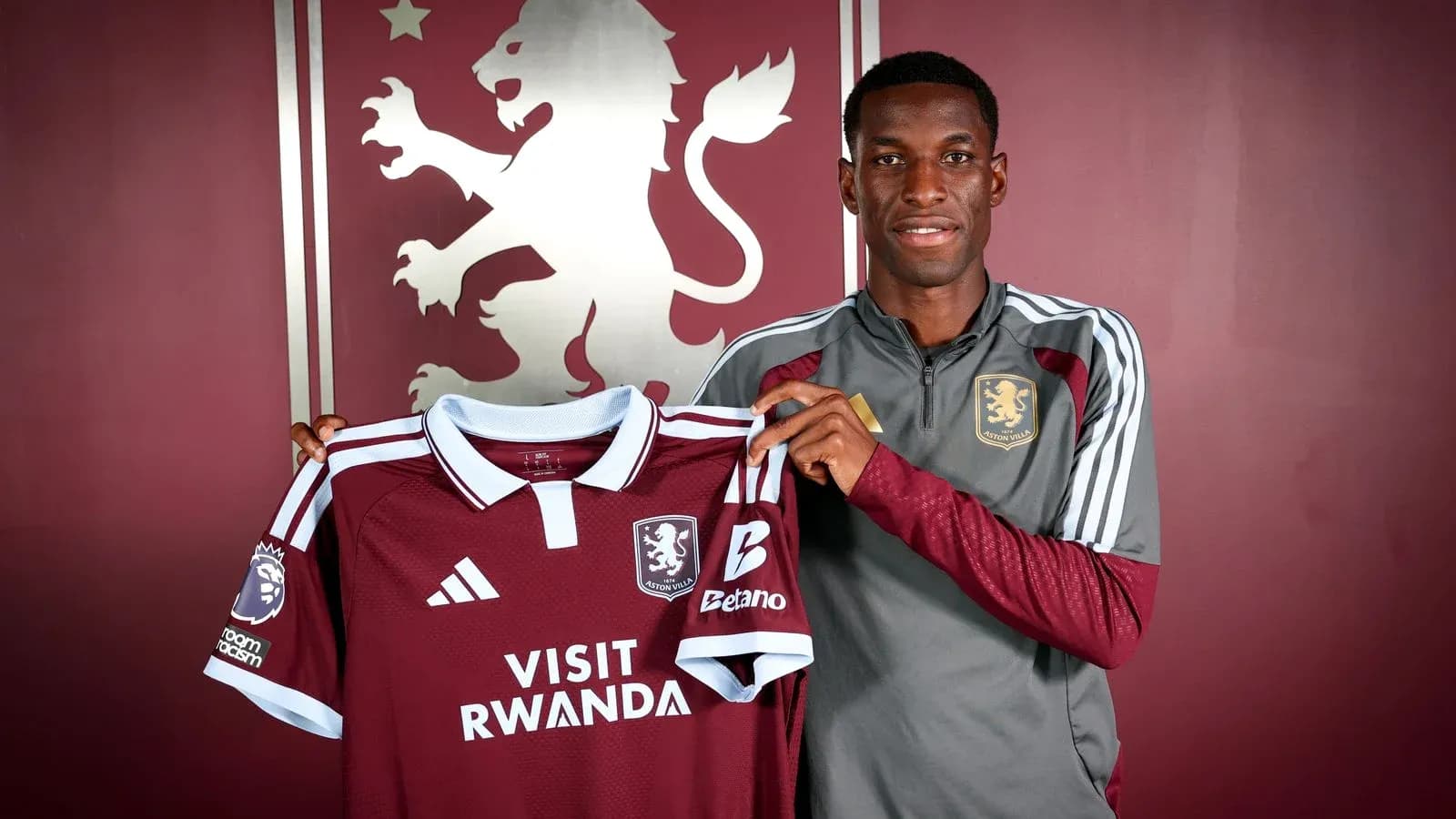 Игрок держит футболку Aston Villa на фоне логотипа Игрок держит футболку Aston Villa на фоне логотипа